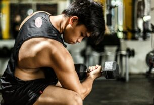 Young man intensely lifting a dumbbell in a gym, highlighting strength and focus.